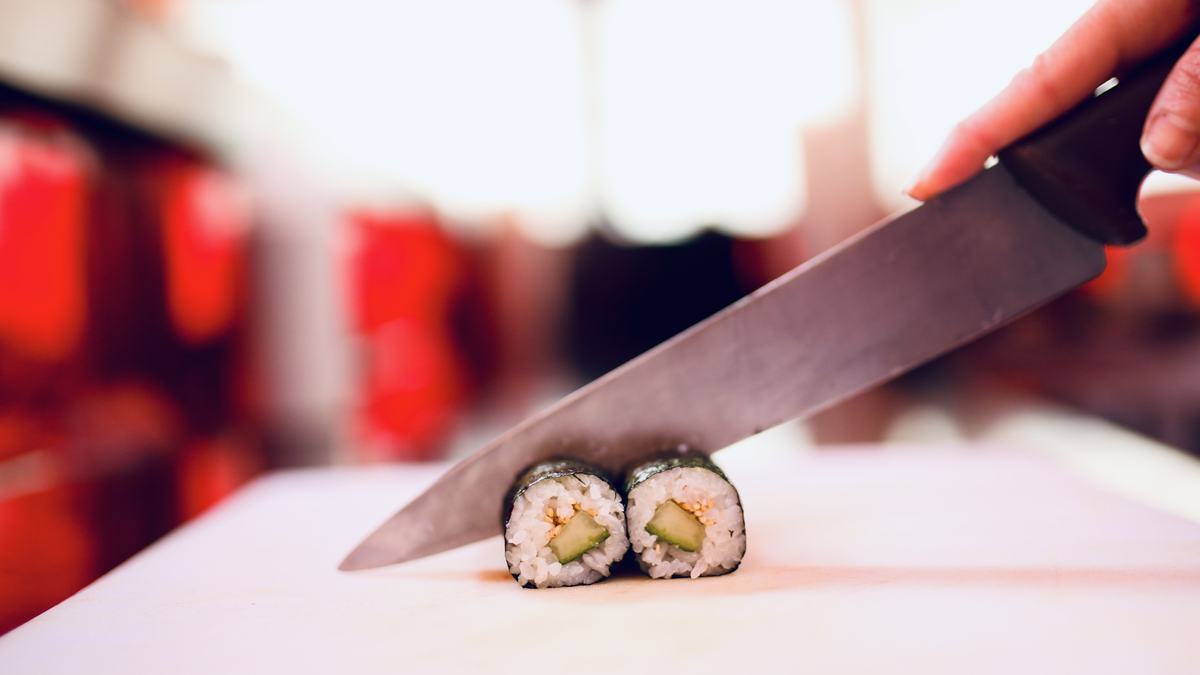 A knife cutting cleanly through a kappa maki roll on a white board