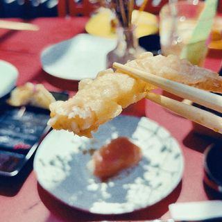 A tempura prawn lifted on chopsticks over the plate