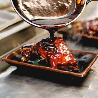 Teriyaki sauce being ladled over a dish at the pass