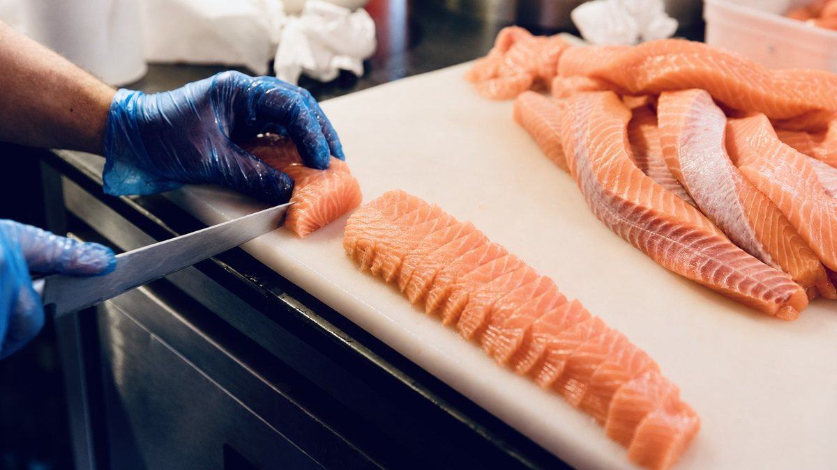 A chef slicing salmon by hand on the board, fillets waiting beside
