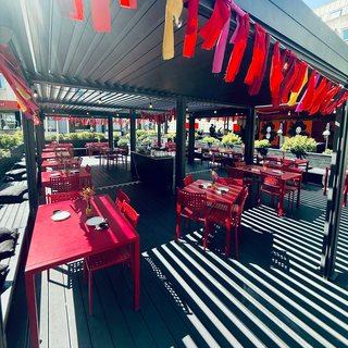 The deck in full sun, red tables under the bunting and the slatted roof